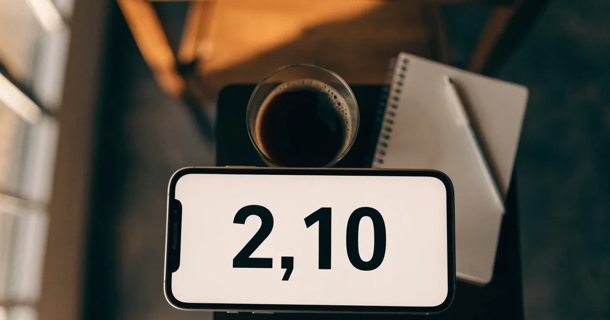 Ein Smartphone mit dunklem Bildschirm liegt auf einem Tisch in einem Café, daneben eine Tasse und ein Notizbuch.
