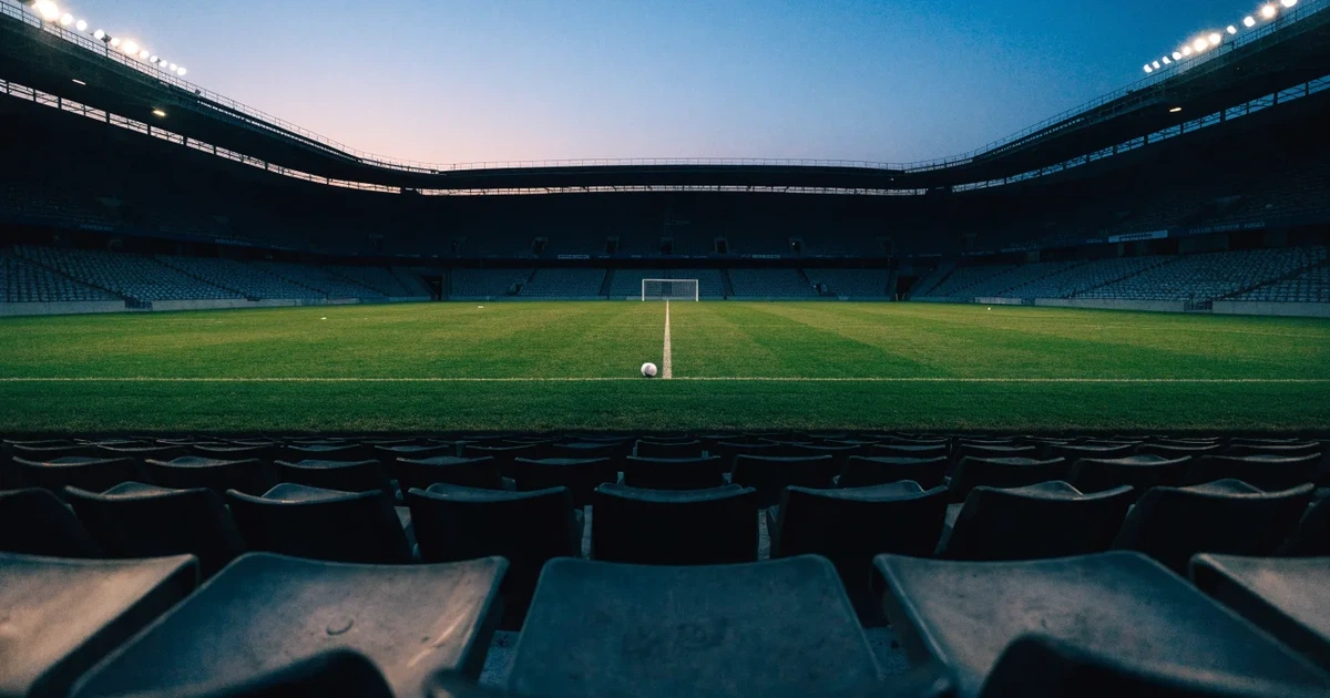 Leere Sitzreihen eines großen Stadions unter Flutlicht, dahinter die ferne Sicht auf den hell beleuchteten Rasen nach Sonnenuntergang.