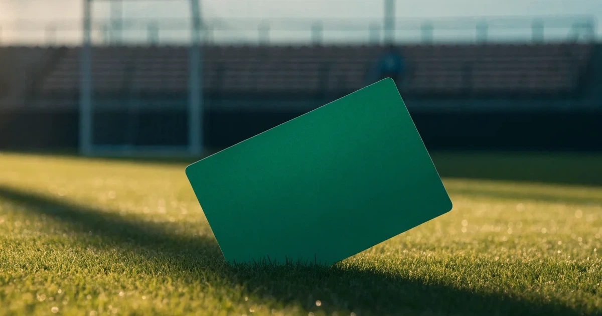 Ein verschlossener leerer Briefumschlag liegt neben einem Fußball auf grünem Rasen im warmen Licht des Nachmittags.