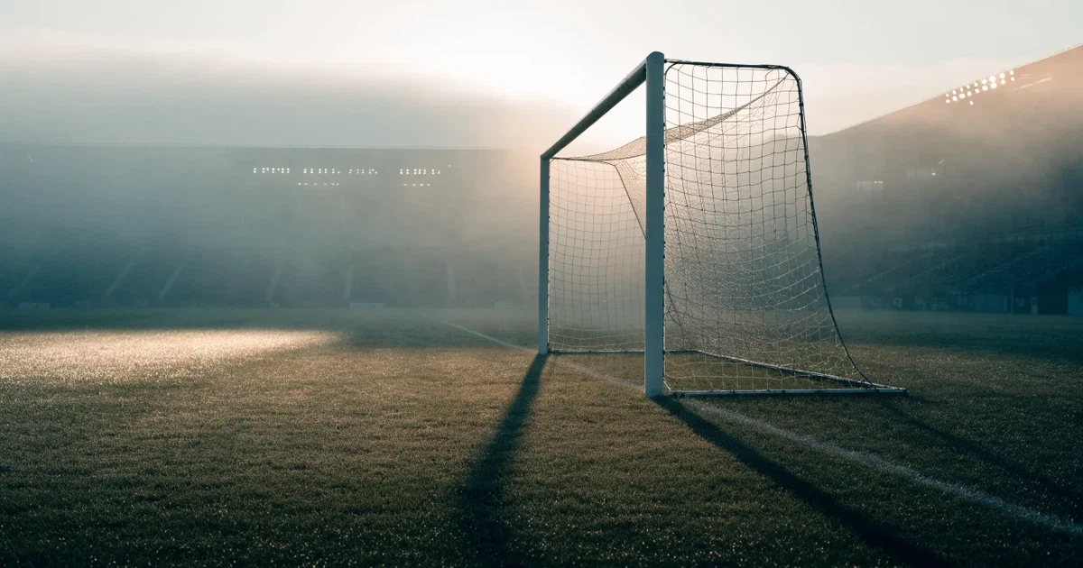 Ein Fußballtor mit Netz steht auf einem leeren Platz im Nebel der Morgendämmerung, der Rasen ist taufeucht.