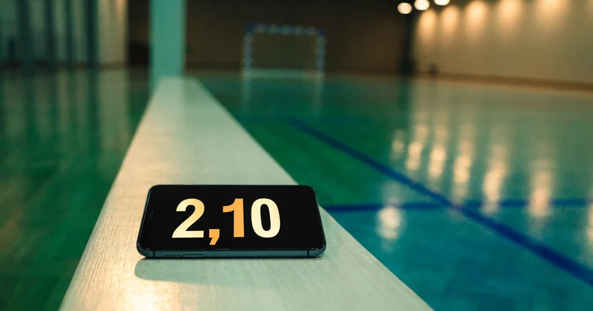 Eine leere Sporthalle mit hellem Hallenboden, kleinen Toren an beiden Enden und blauen Linien, Licht fällt von oben.
