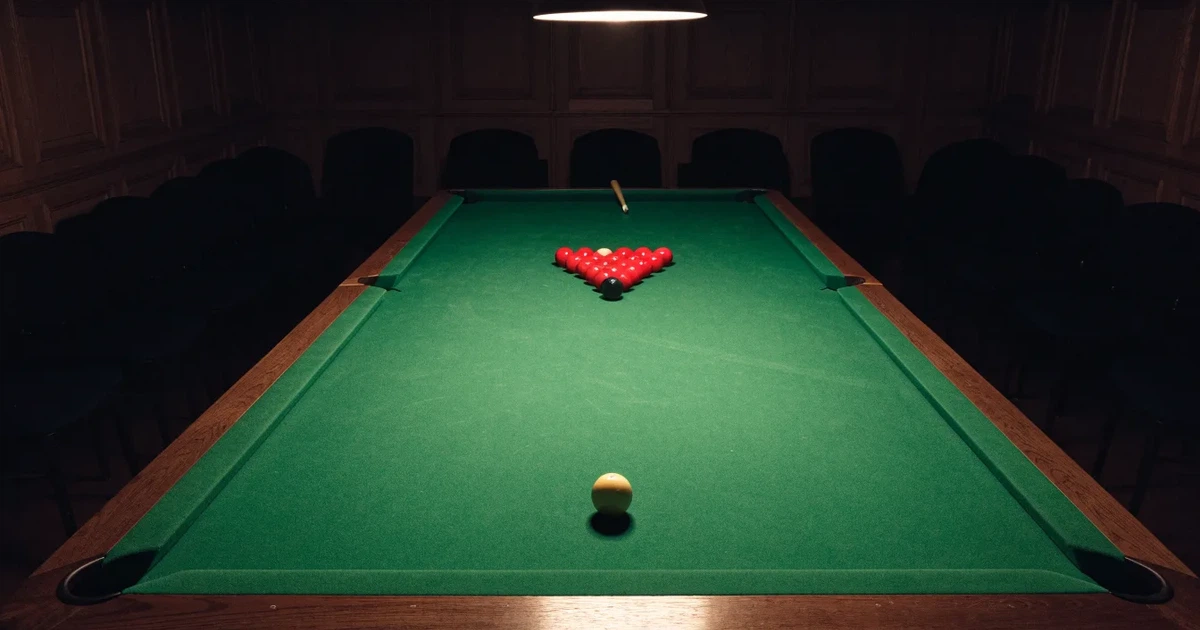 Ein Snookertisch mit grünem Tuch und aufgebauten roten Kugeln in einem abgedunkelten Raum unter einer hängenden Lampe.