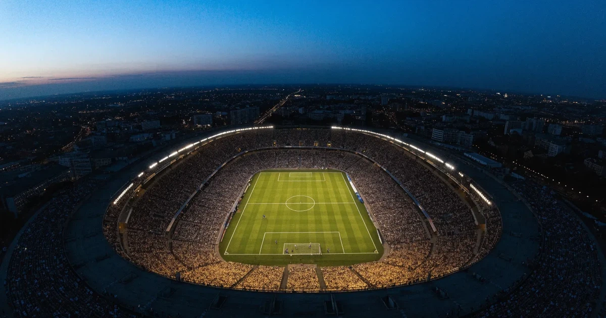 Ein riesiges Stadion in der Abenddämmerung aus der Vogelperspektive gesehen, die Lichter an den Rängen sind eingeschaltet.