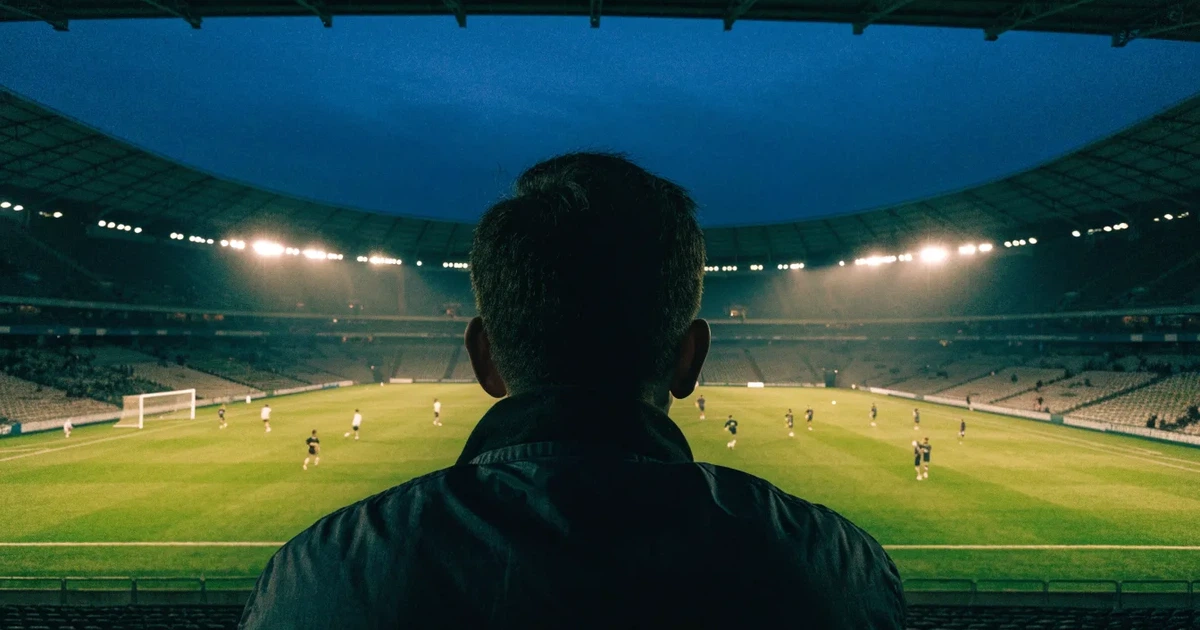 Ein großes Fußballstadion mit hell erleuchtetem Rund, aus der Ferne am Abend gesehen, davor eine breite Allee mit Laternen.